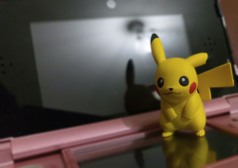 Pikachu standing in front of a pink Nintendo 3DS